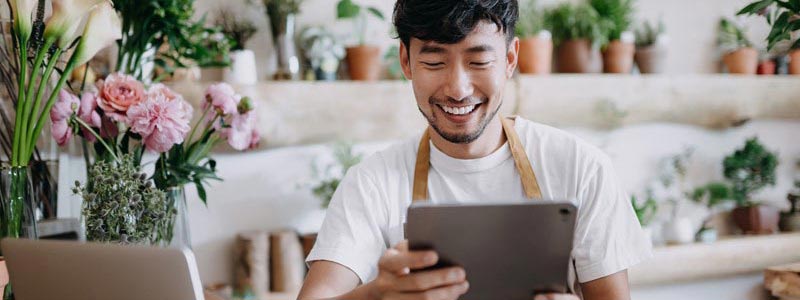 Flower shop owner smiling and looking at tablet.