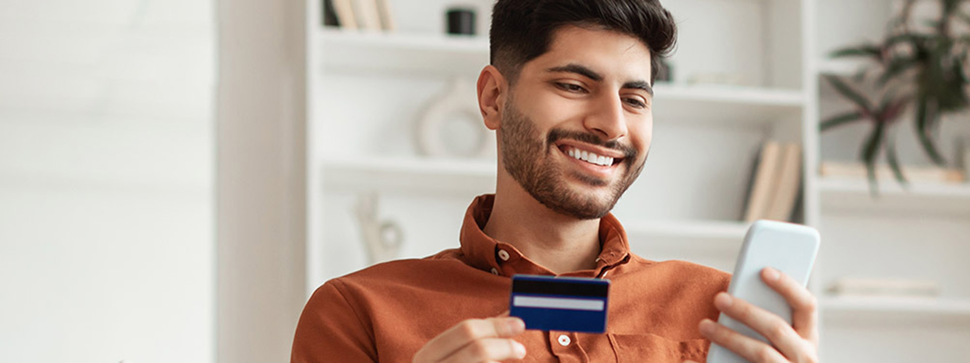 Hombre sonriendo mientras usa su teléfono y sostiene una tarjeta 