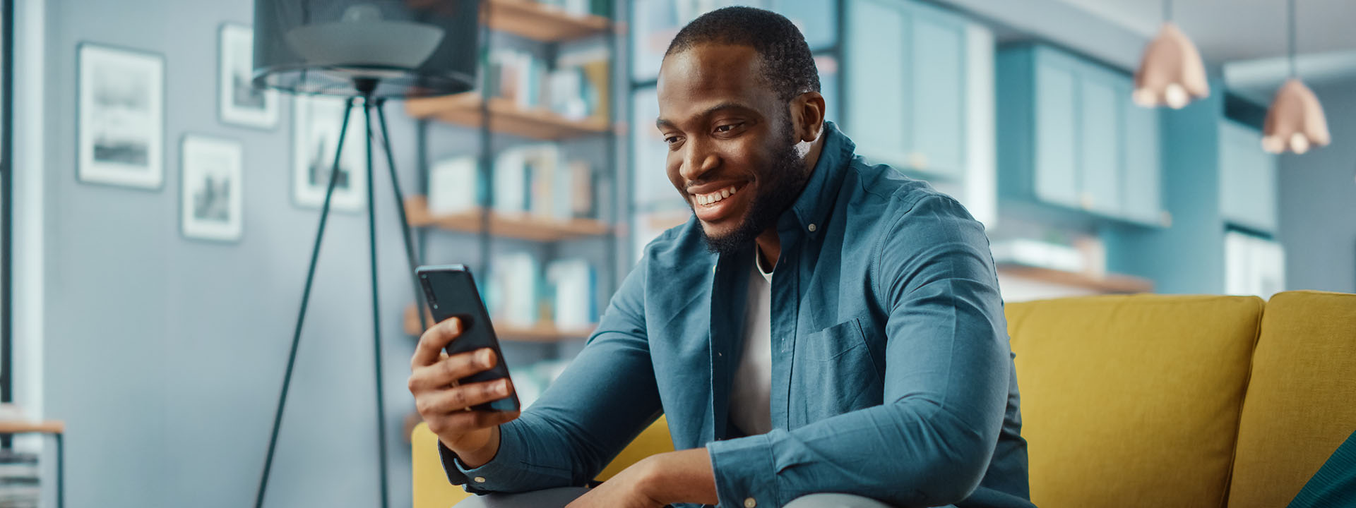 Hombre sentado en el sillón de su casa sonriente mirando su celular