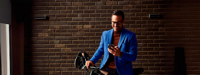 Hombre sonriente usando su celular sosteniendo su bicicleta