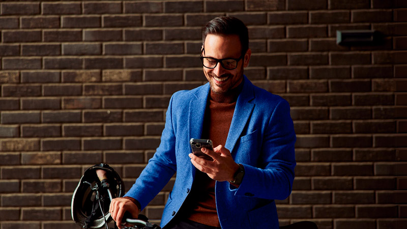 Hombre sonriente usando su celular sosteniendo su bicicleta